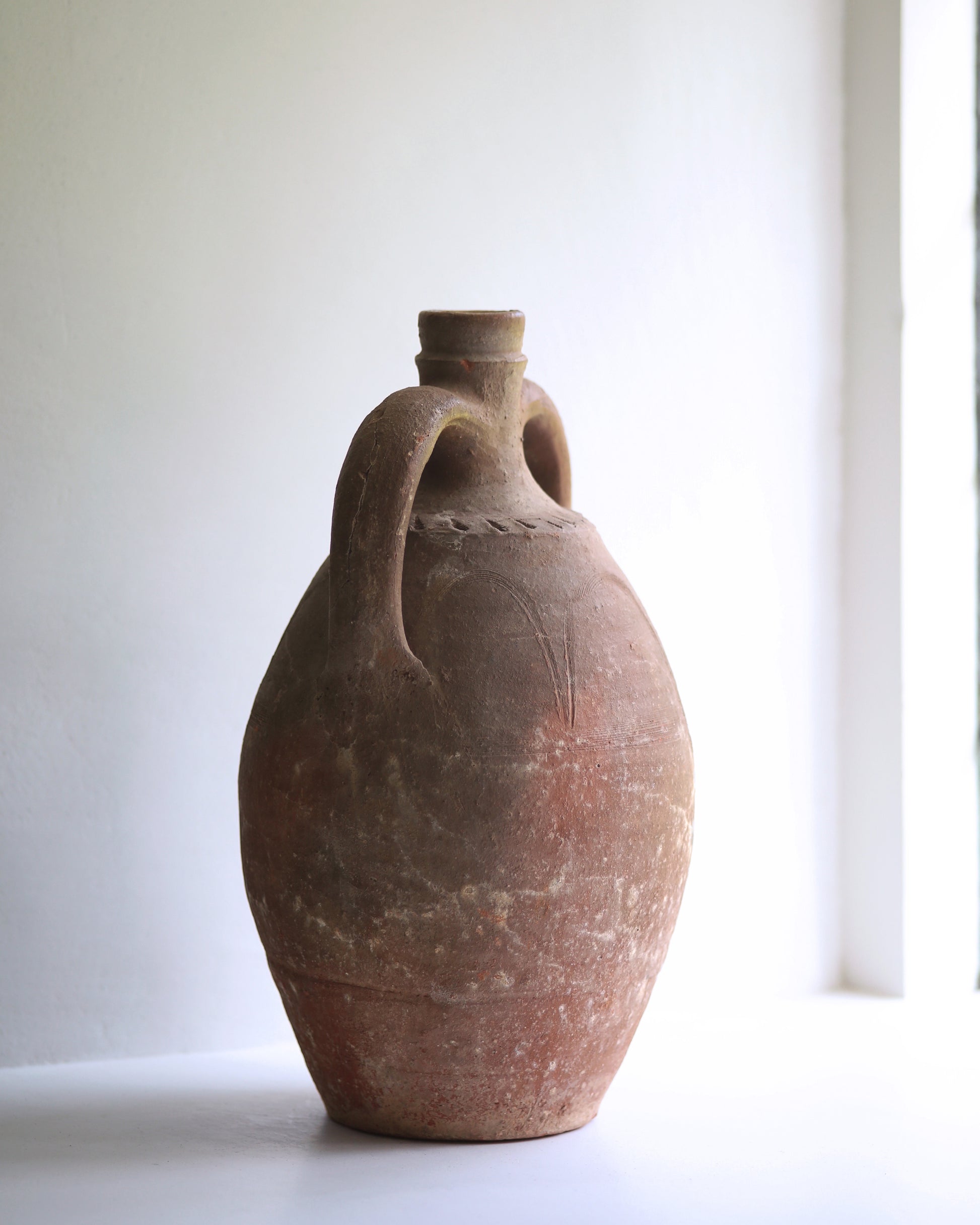 Side of large handled amphora in window sill showing deep hand-carved decorative details