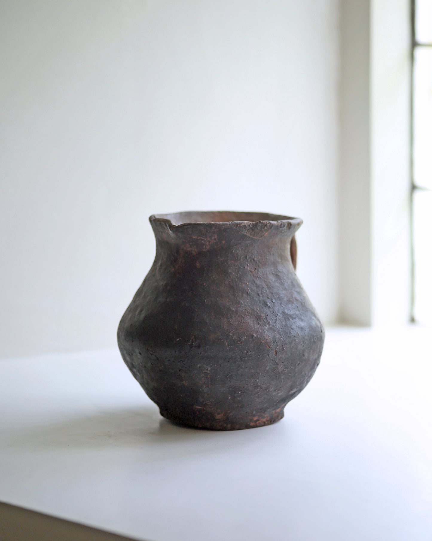 Hand thrown organic shape rustic clay jug in dark baked terracotta