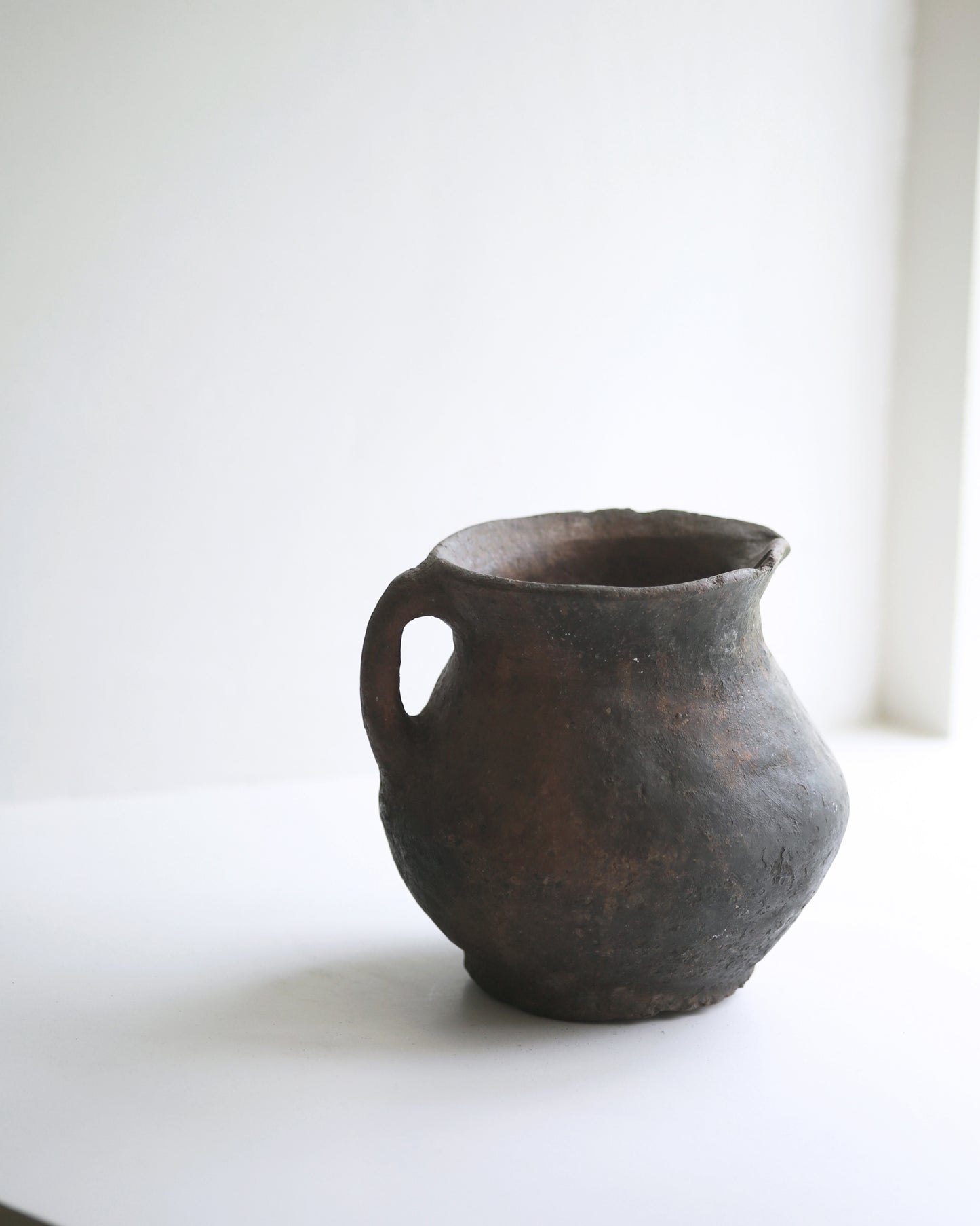 Dark aged terracotta pottery jug in neutral interior