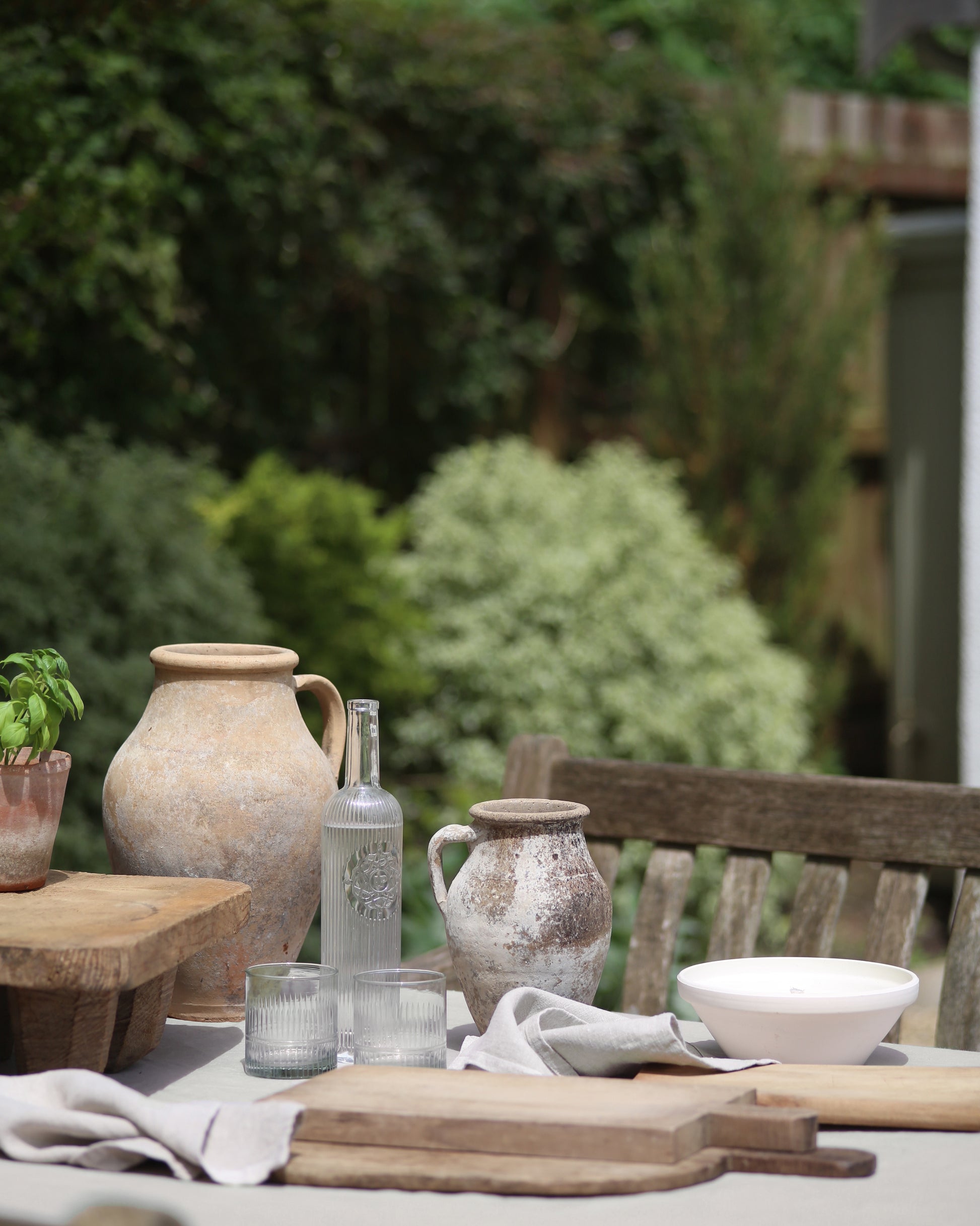 Antique terracotta pottery and vintage breadboards displayed in al fresco garden dining setup