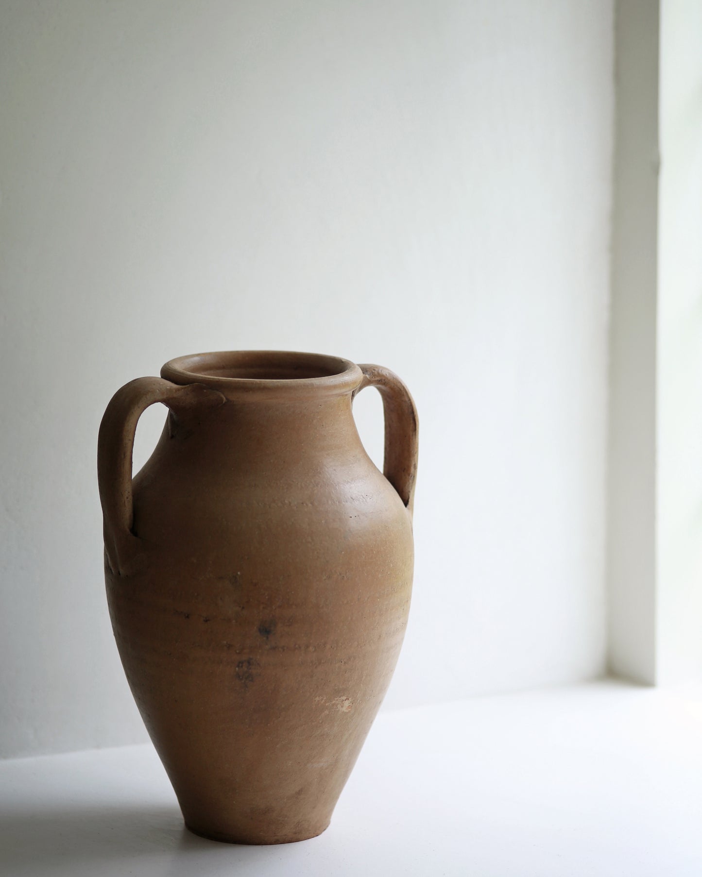 Vintage terracotta urn displayed on a sunny window sill