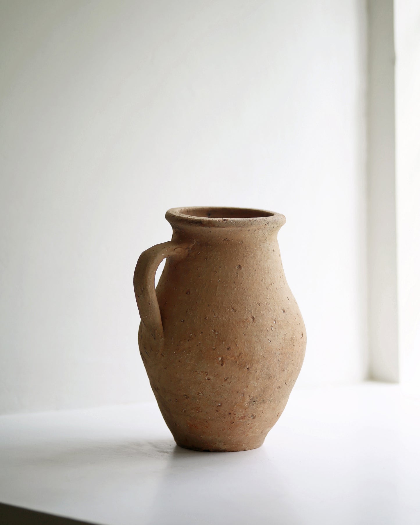 Small vintage pale terracotta pot displayed on a sunny window sill