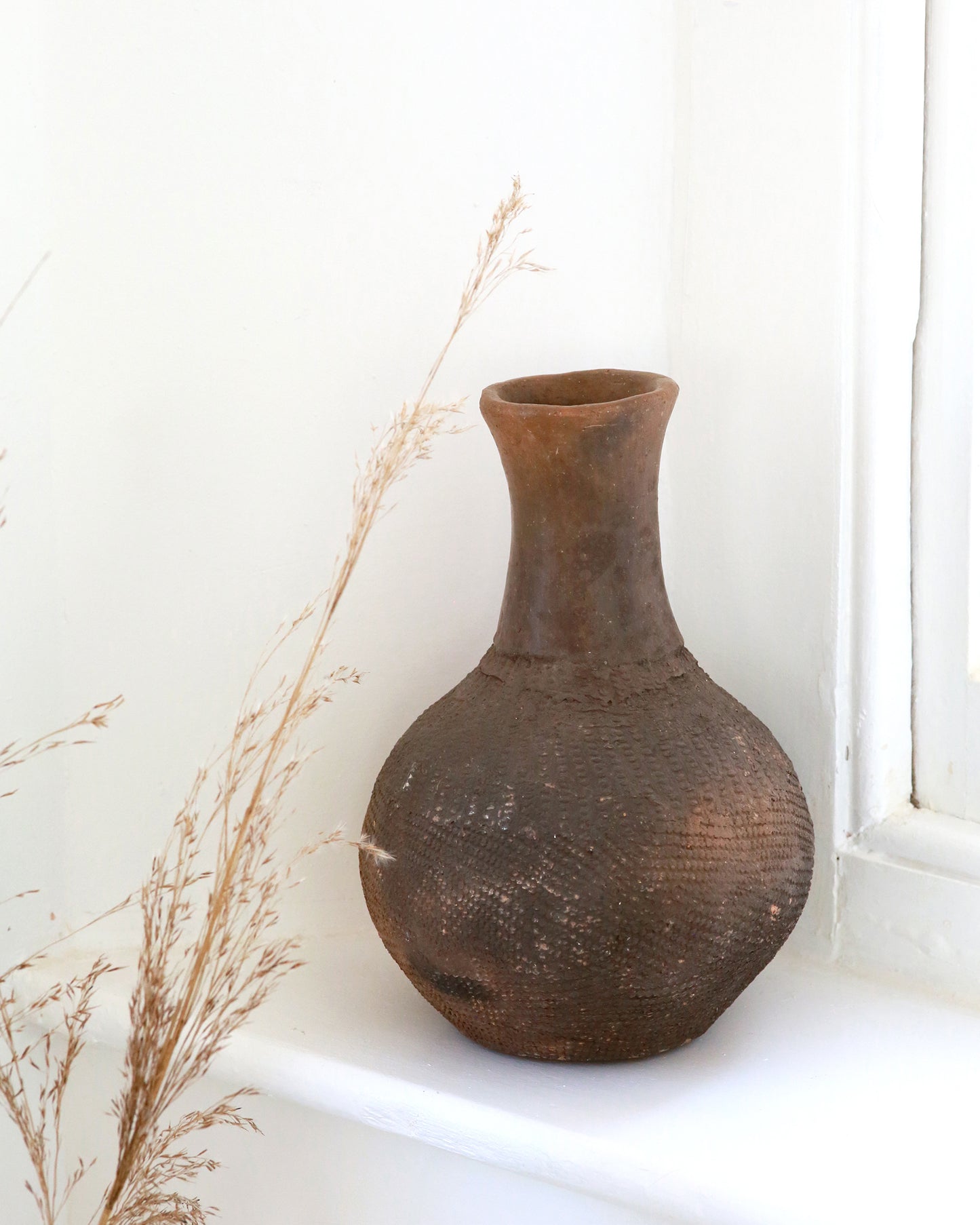 Antique African textured vase on window sill with natural stems